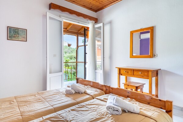A bedroom with two beds, a wooden headboard, a small wooden table, a mirror, and an open door leading to a balcony. - Studio Apartment 'Maltas  17' with Shared Terrace, Wi-Fi and Air Conditioning (Corfu)