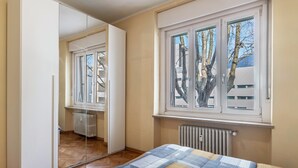 A bedroom with a large mirror, a window with a view of trees, a radiator, and a bed with a quilt.