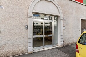 Une entrée d’immeuble avec une porte en verre, un mur en briques et une voiture jaune garée à l’extérieur.