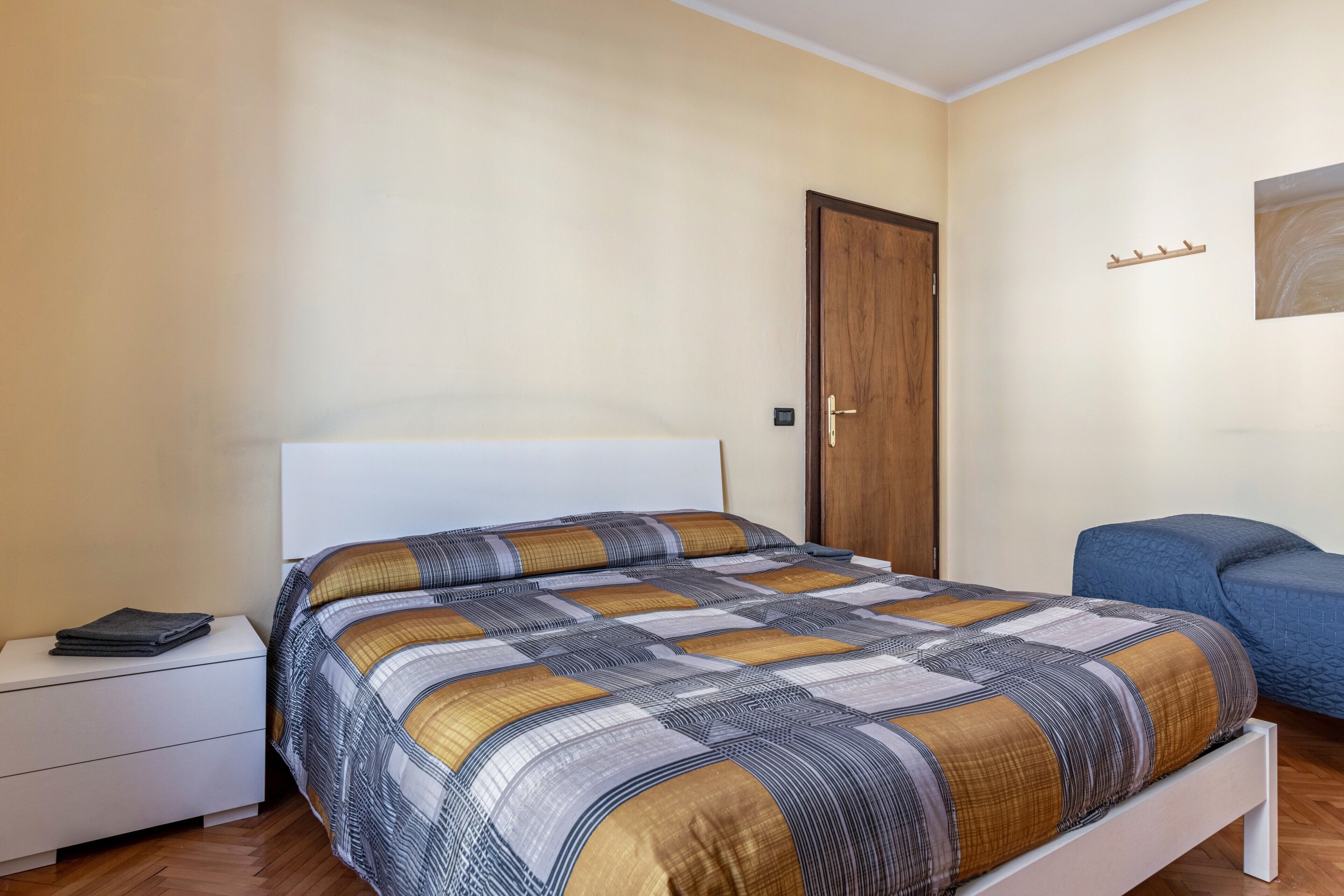 A bedroom with a bed, a nightstand, a wooden door, and a blue chair.