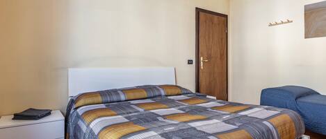 A bedroom with a bed, a nightstand, a wooden door, and a blue chair.