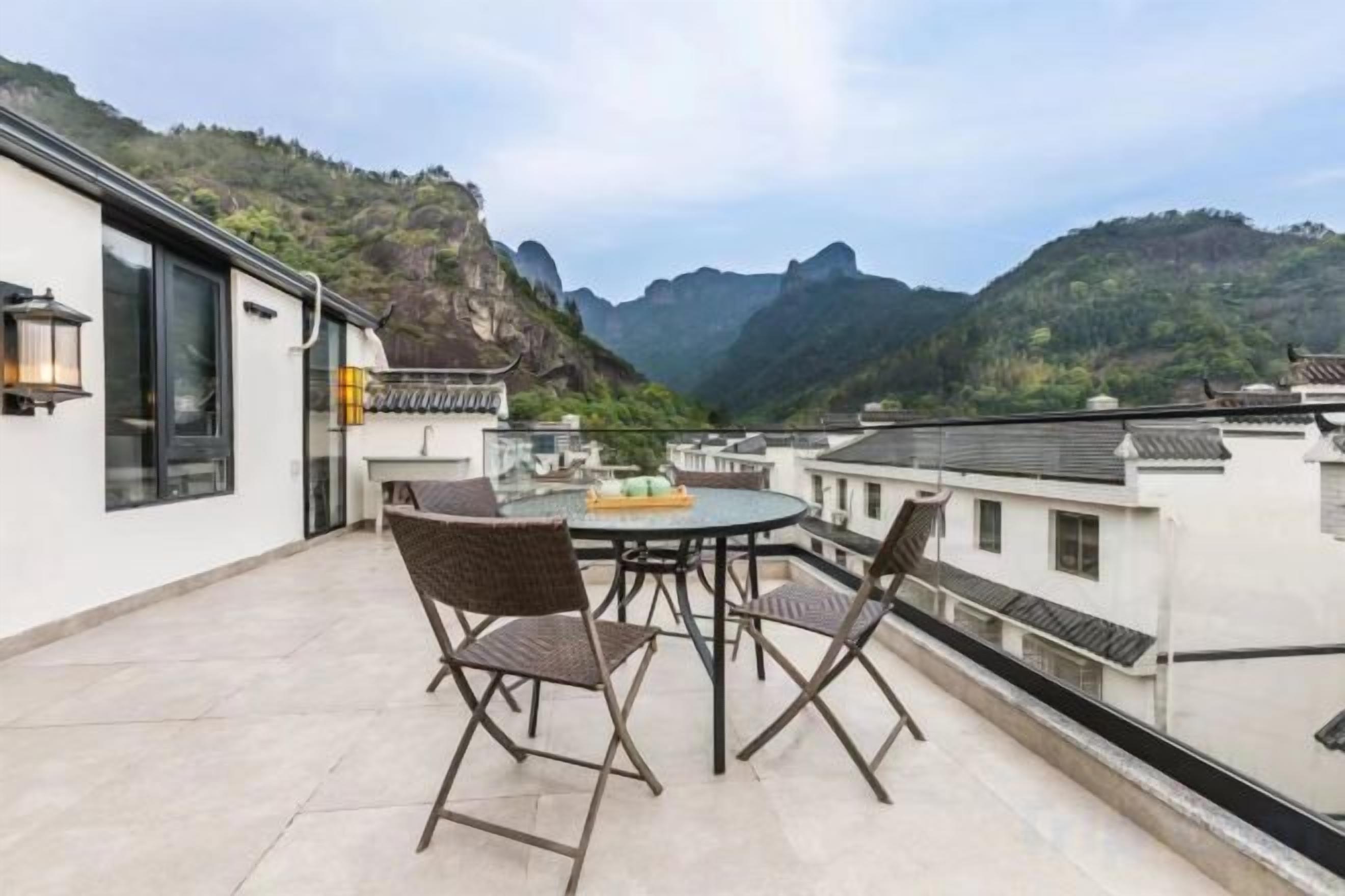A balcony with a round table and chairs, overlooking a mountainous landscape.
