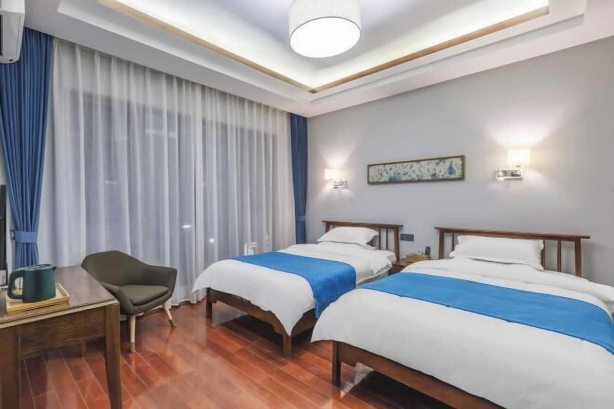 A hotel room with two beds, a desk, a chair, and a large window with curtains.
