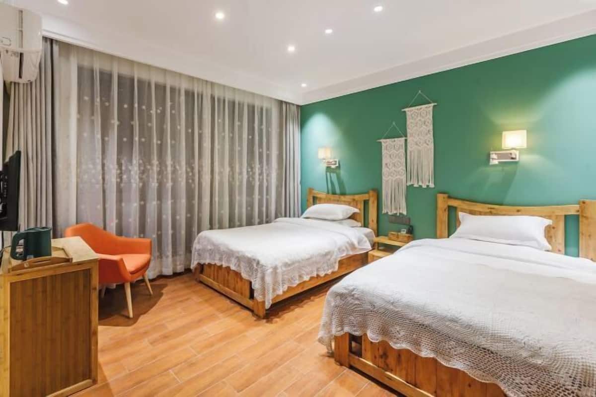 A hotel room with two wooden beds, a wooden desk, an orange chair, and a green accent wall.