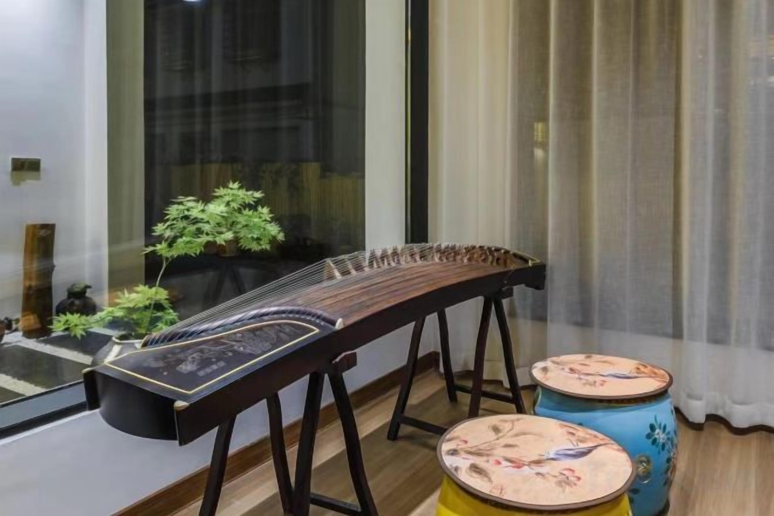 Un instrument à cordes traditionnel posé sur un support, une petite plante en pot et deux tambours décoratifs.