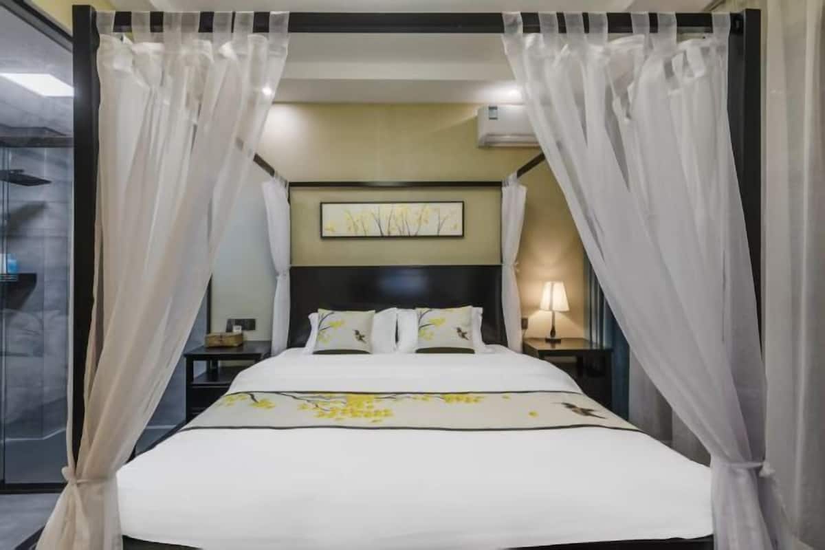 A hotel room with a bed, a nightstand, a lamp, and a wall-mounted artwork.