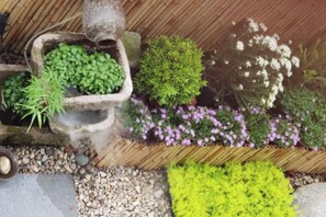A garden with various plants and flowers, including a stone planter with green foliage and a wooden planter with purple flowers. - Tingxiju Inn (Xianju)
