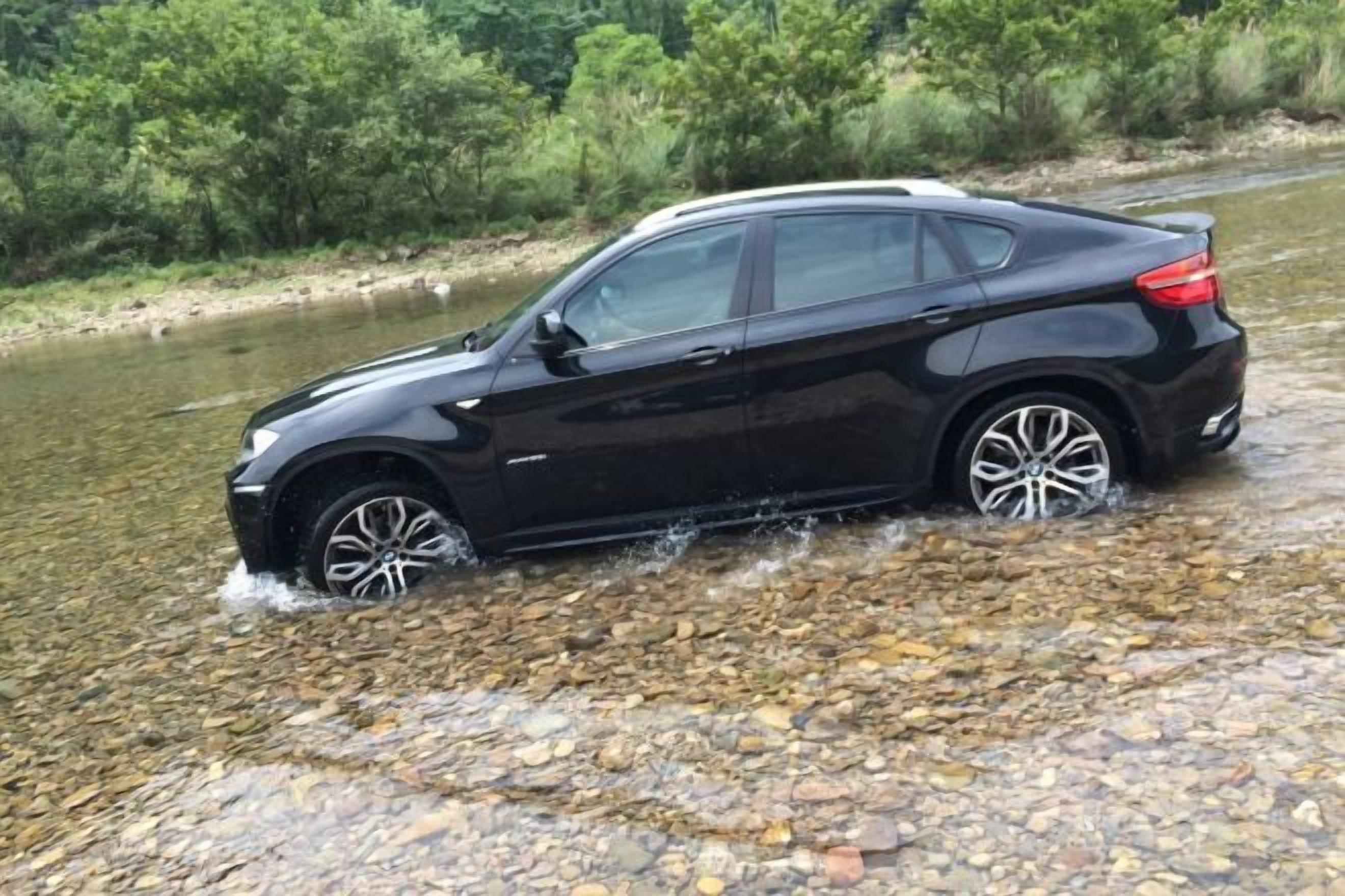 A black car driving through a shallow stream.