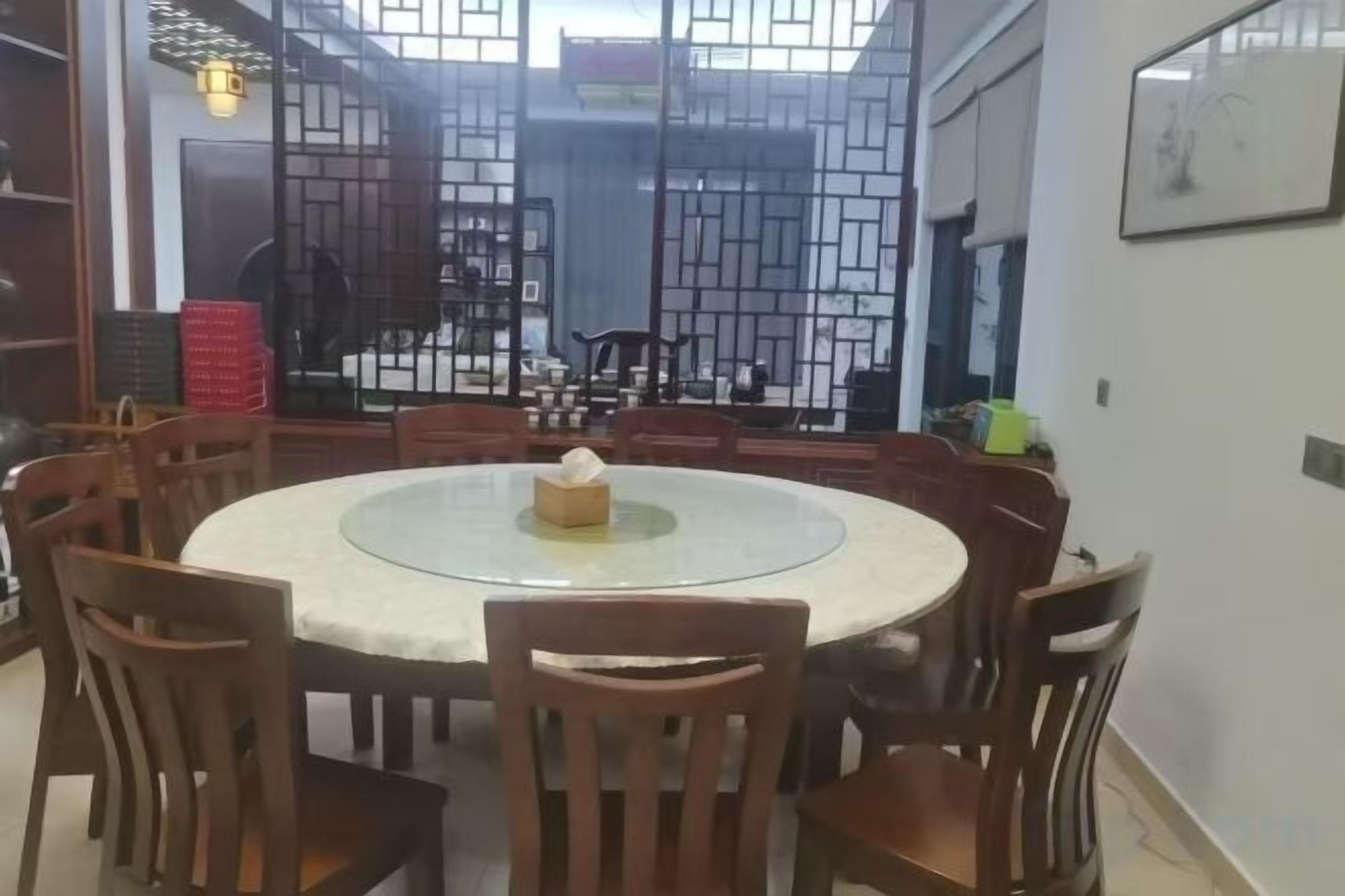 A round dining table with chairs, a tissue box, and a view through a lattice partition to a balcony.