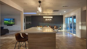 Een moderne keuken met een groot eiland, een zithoek met stoelen, een neonbord en een tv waarop een landschap te zien is.