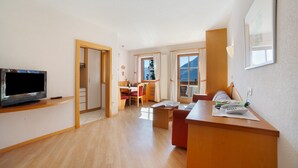 A modern living room with a flat-screen TV, wooden furniture, a dining area, and large windows. - Wiedmairhof Apartment 'Grafensteiner' with South/east facing balcony, Shared Terrace, Garden & Wi-Fi (Lagundo)