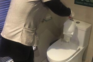 A person cleaning a toilet with a spray bottle. - Anna Baige Hotel (Shanghai)