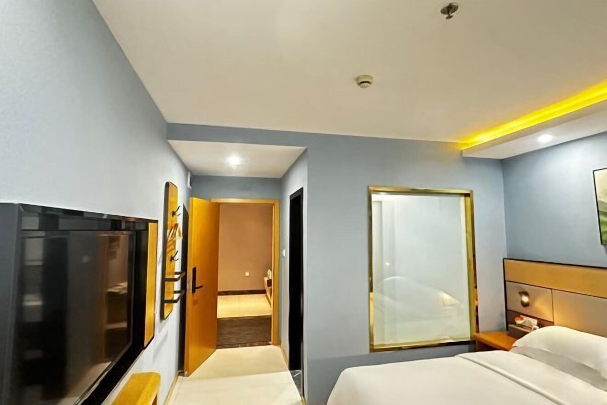 A hotel room with a bed, a TV, a bedside table, and a mirror.