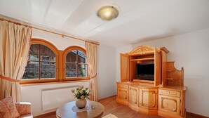 A room with a wooden cabinet, a television, a round table with a vase, and a sofa. - Wiedmairhof Apartment 'Schwalbennest' with West-facing balcony, Shared Terrace & Garden and Wi-Fi (Lagundo)
