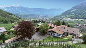 A mountainous village with traditional houses, a large tree, and a view of distant mountains. - Wiedmairhof Apartment 'Schwalbennest' with West-facing balcony, Shared Terrace & Garden and Wi-Fi (Lagundo)