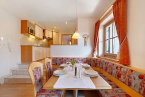 Un espace repas avec une table en bois, des bancs et une cuisine en arrière-plan.