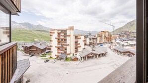 A view of a mountain resort with multi-story buildings, a parking area, and a construction crane in the background. - Apartment '6p Au Pied Des Pistes' with Mountain View, Balcony and Wi-Fi (Val Thorens)