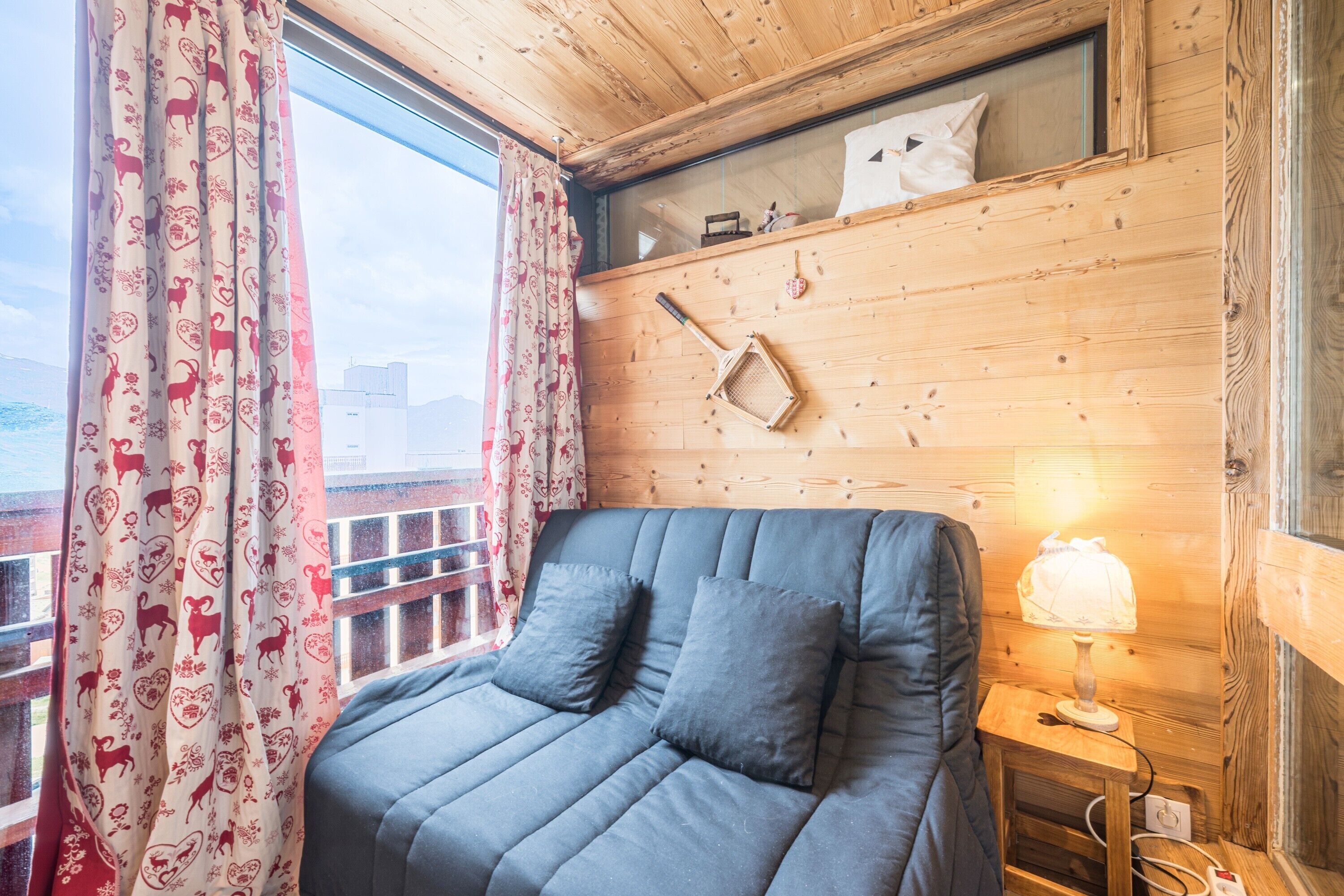Een kamer met een bed, een raam met gordijnen, een lamp en een houten wand met een plank.