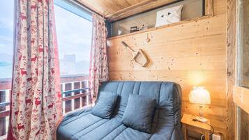 Een kamer met een bed, een raam met gordijnen, een lamp en een houten wand met een plank.