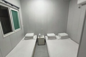 A small, single-room hotel room with two beds, a window, and a wall-mounted air conditioning unit. - Xinyue Hotel (Taiyuan Ophthalmology Hospital) (Taiyuan)