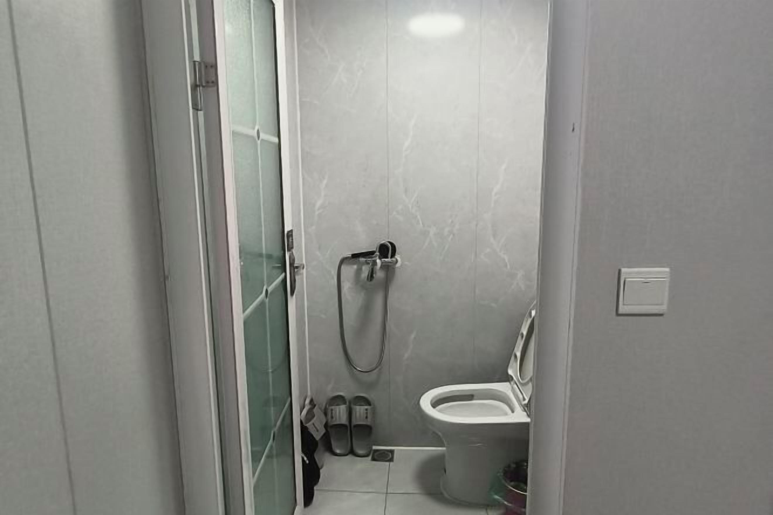 Un baño pequeño con inodoro, ducha y puerta de vidrio que da a un pasillo.