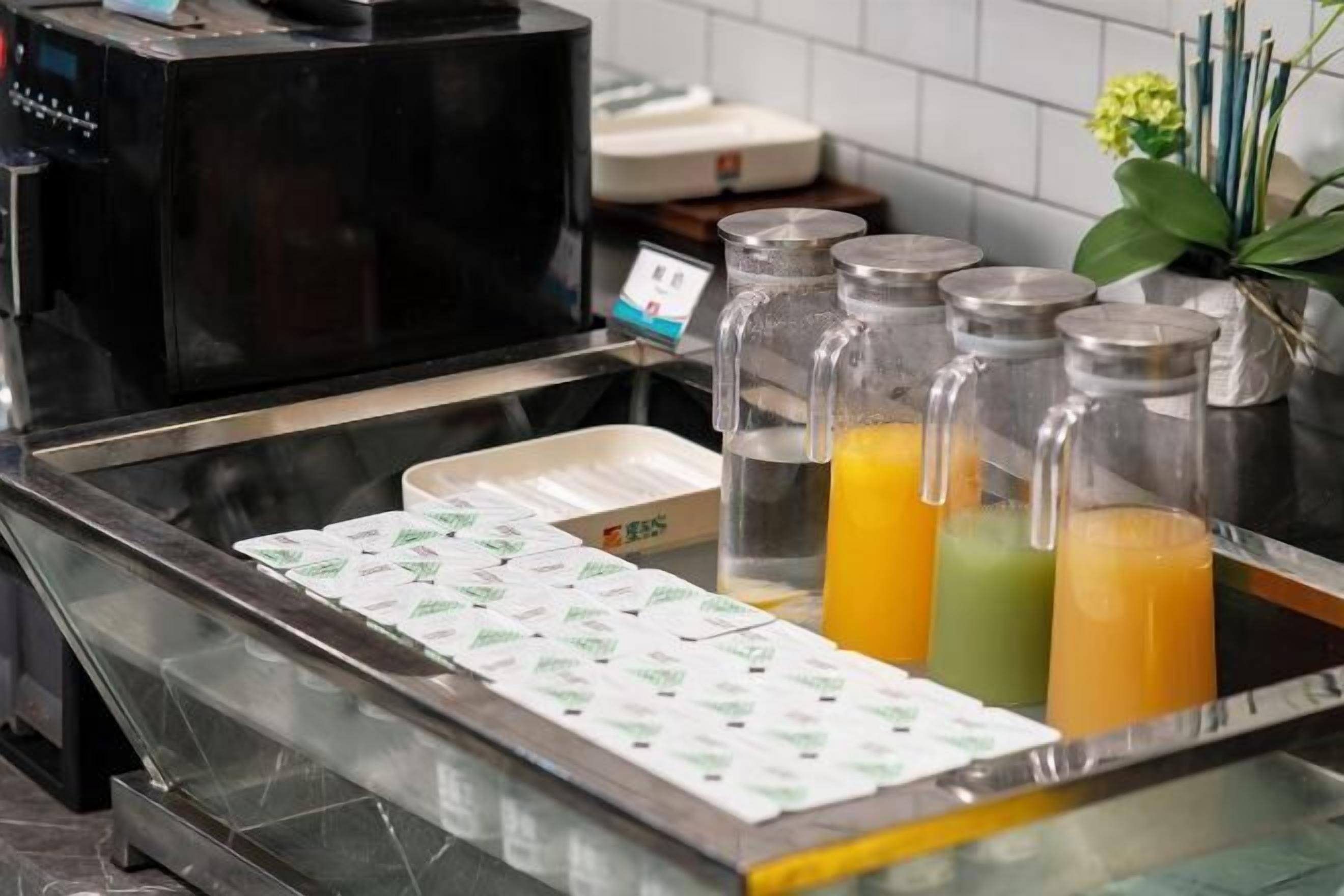 A beverage station with a coffee machine, juice dispensers, and a tray of packaged items.