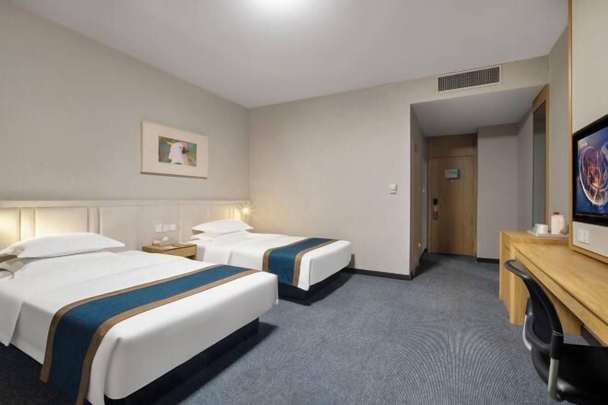 A hotel room with two beds, a desk, a chair, and a television.