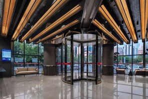A lobby with a revolving door, a sofa, and a glass wall with a city view. - Jinjiang Inn (Zhengzhou High-speed Railway East Station Zhengdong MixC Branch) (Zhengzhou)