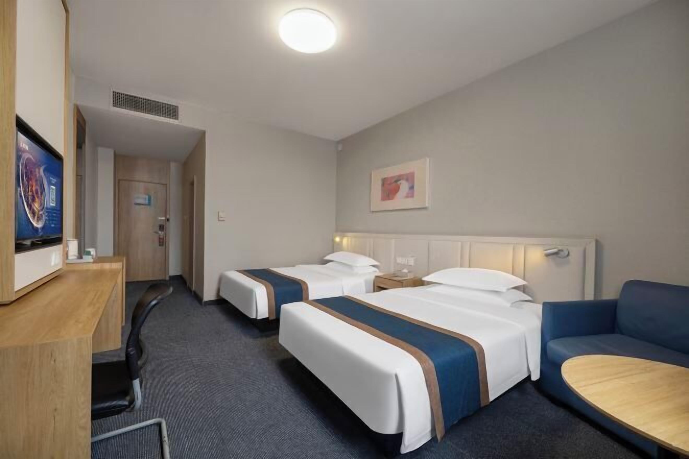 Ein Hotelzimmer mit zwei Betten, einem Schreibtisch, einem Sessel, einer Couch und einem Fernseher.