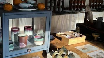 A display of ceramic items, including cups and teapots, on a wooden table with a glass-fronted cabinet.