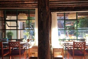 Un comedor con muebles de madera, ventanas amplias y vista a la vegetación exterior.