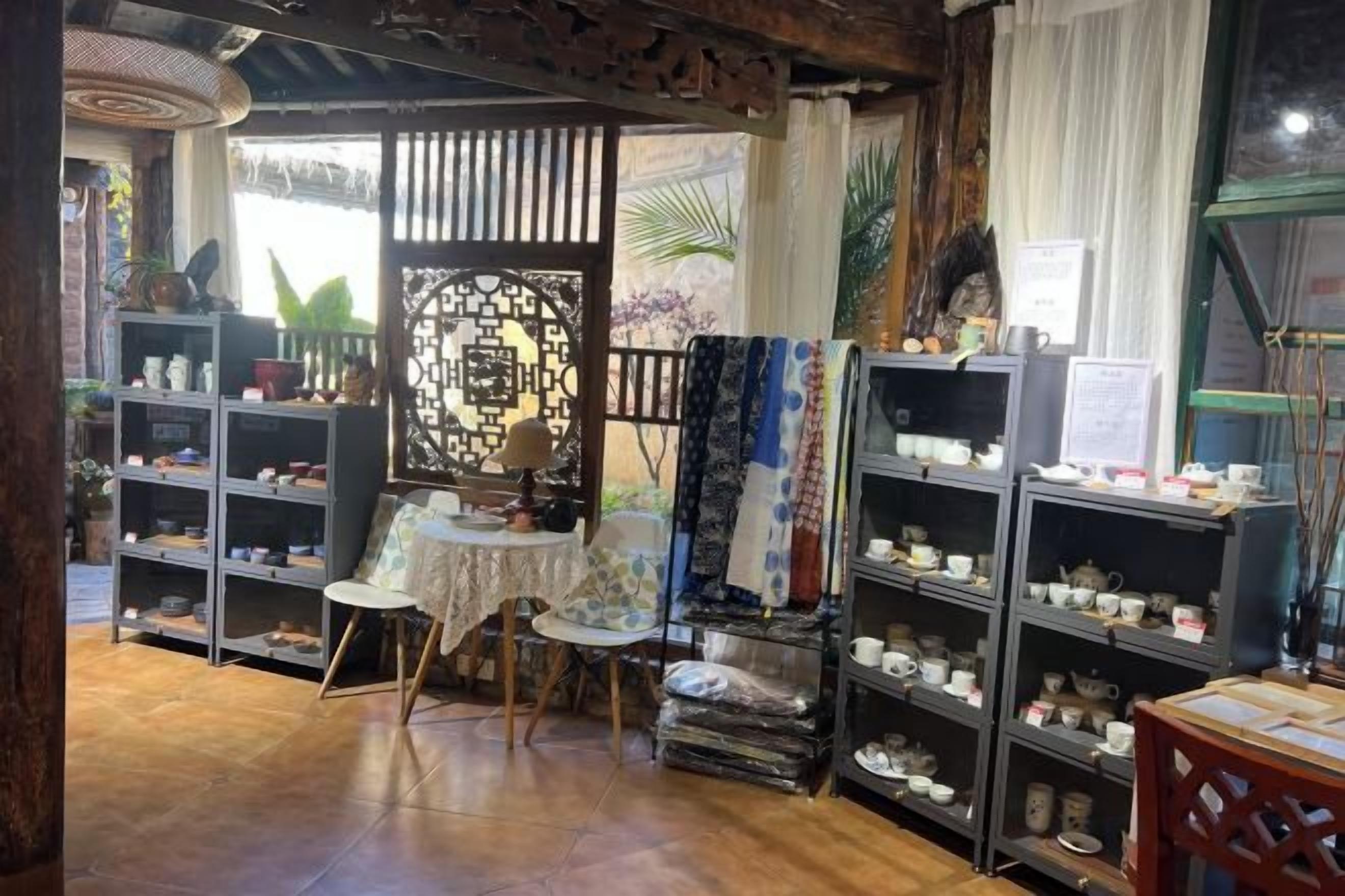 A room with shelves of ceramics, a small table, and a chair.