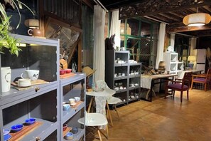 A room with shelves of pottery and ceramics, a dining table with chairs, and a large window with curtains.