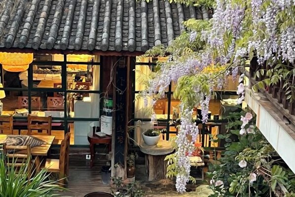 Um edifício em estilo japonês tradicional, com telhado de telhas, mobiliário de madeira e flores roxas penduradas.