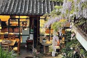 Un edificio tradicional japonés con tejado de tejas, muebles de madera y flores moradas colgantes.