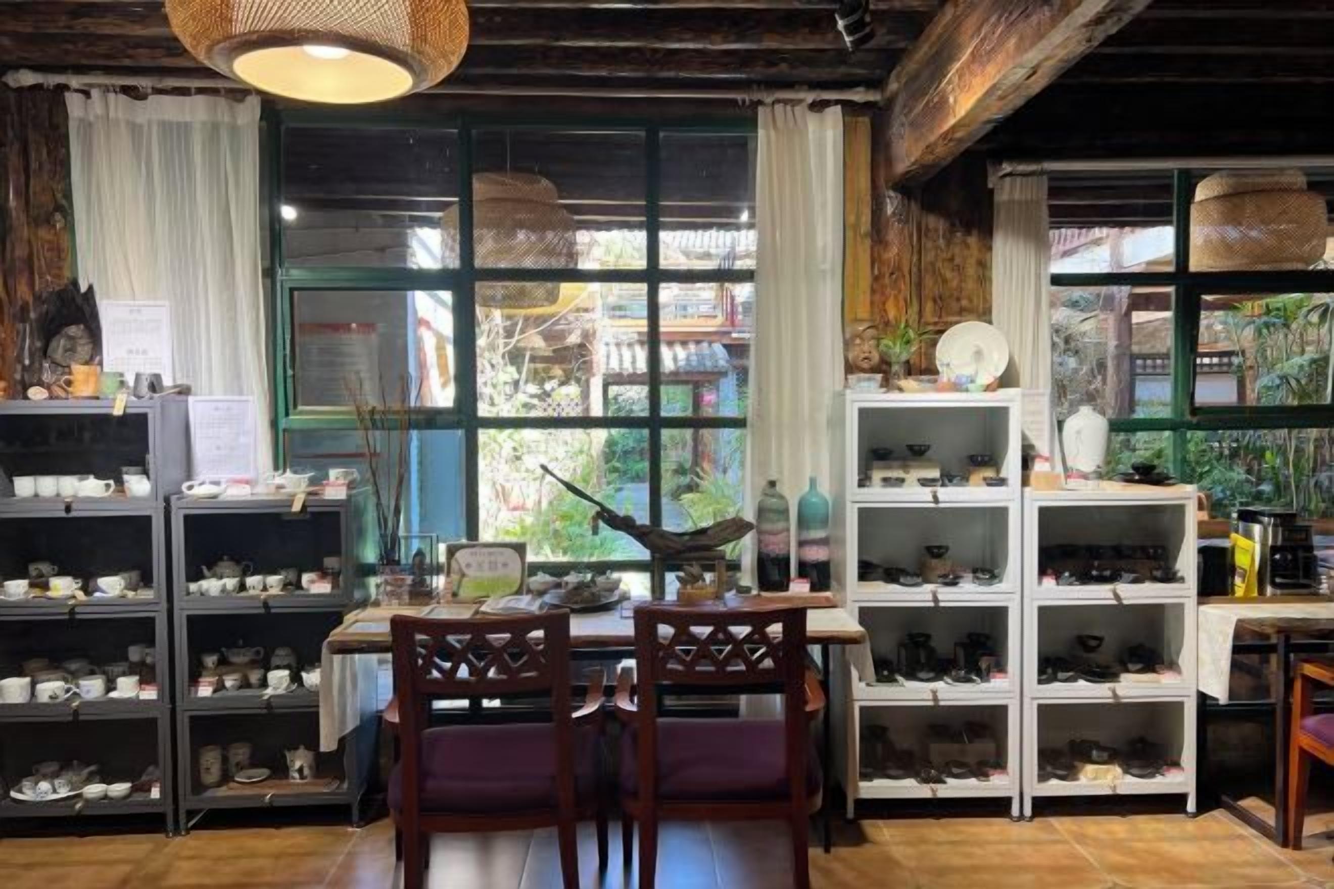 A room with a wooden ceiling, a dining table with chairs, shelves with shoes, and a large window with curtains.