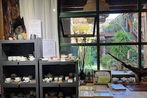 A tea shop with shelves of teapots and cups, a menu, and a view of a traditional courtyard.
