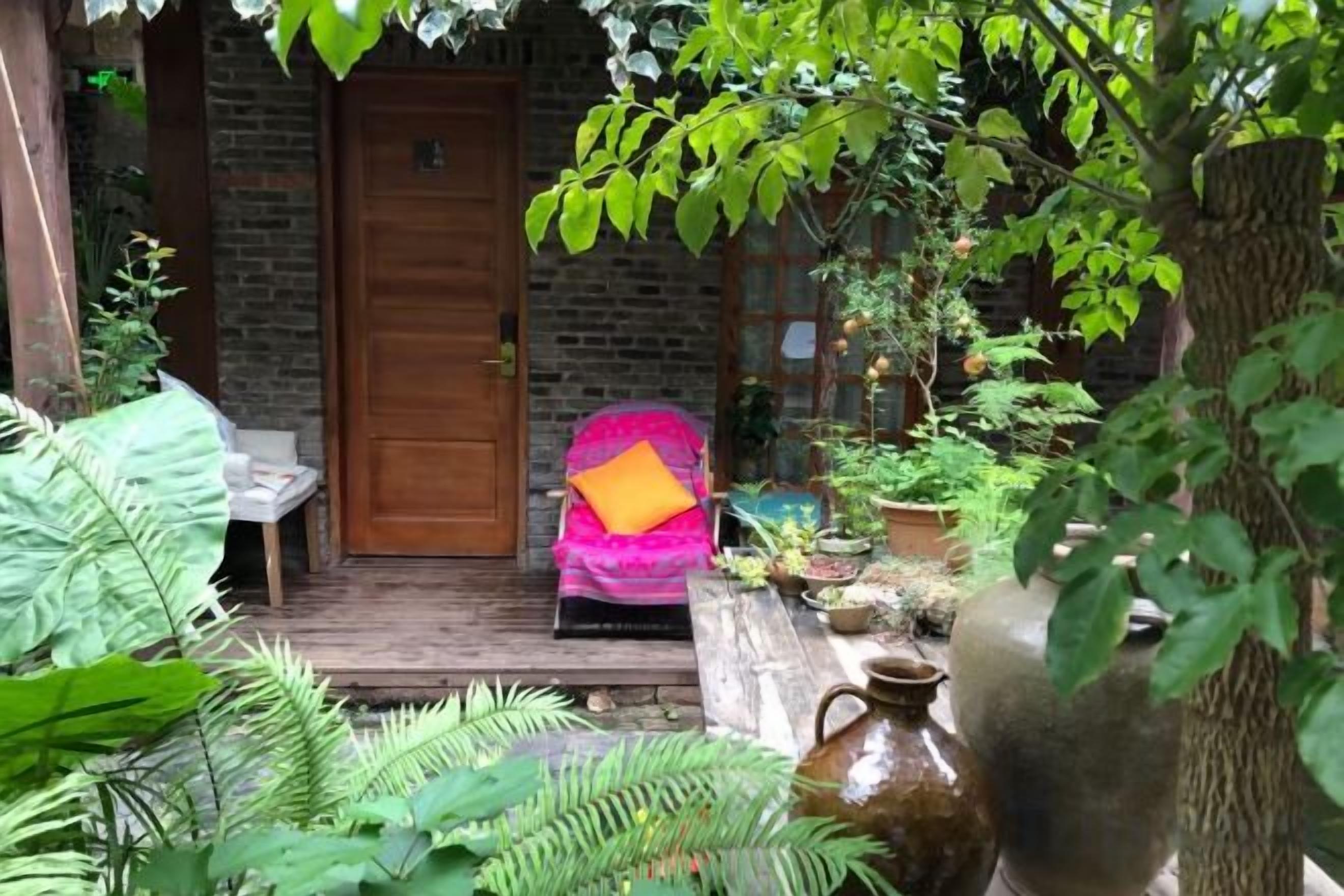 A wooden porch with a brick wall, a wooden door, and a chair with a cushion.