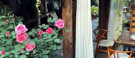 A wooden table and chairs outside a building with a tiled roof, surrounded by pink roses.