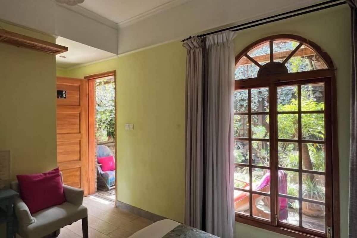 Une pièce avec un lit, une chaise, une fenêtre avec des rideaux et une porte donnant sur l’extérieur.