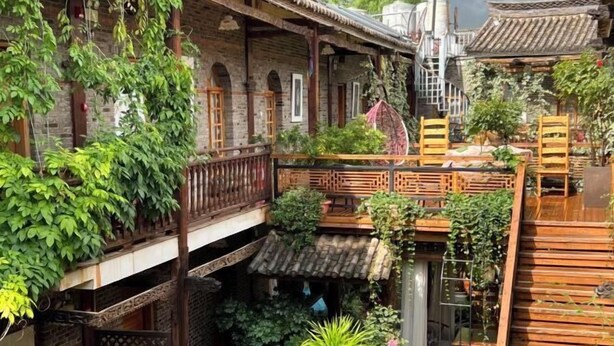 A traditional courtyard with wooden balconies, potted plants, and a small seating area. - Yunguichu Chain Inn (Jianchuan)