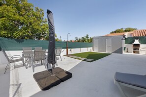 Eine Außenpatio mit Tisch und Stühlen, einem schattenspendenden Sonnenschirm und einer kleinen Rasenfläche.