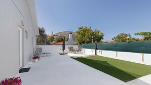 Ein weißes Gebäude mit einer Terrasse, Gartenmöbeln und einem grünen Rasen.