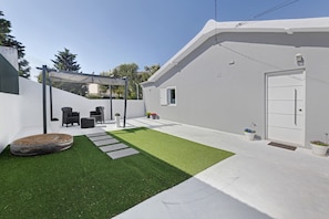A modern house with a white exterior, a patio with artificial grass, outdoor furniture, and a pergola.