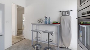 Eine moderne Küche mit einem Edelstahlbackofen, einem kleinen Tisch mit zwei Barhocker und einem an der Wand befestigten Bügelbrett.