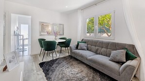 Ein modernes Wohnzimmer mit einem grauen Sofa, grünen Sesseln, einem runden Tisch und einem großen Fenster mit Blick auf Bäume.