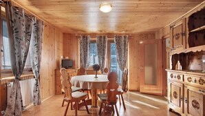 Ein Zimmer mit Holzwänden, einem runden Esstisch, Stühlen, einem Fernseher und einem Schrank.