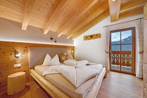 Une chambre aux murs lambrissés, avec un lit, une table de chevet et une vue sur les montagnes par la fenêtre.