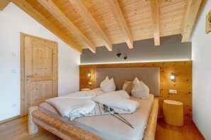 Une chambre avec un plafond en bois, un lit avec une literie blanche, un banc en bois et un petit tabouret rond.