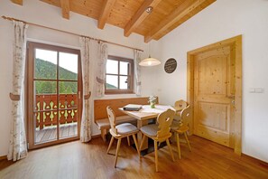 Une table de salle à manger en bois, quatre chaises, un banc, une fenêtre avec des rideaux et une porte avec un cadre en bois.
